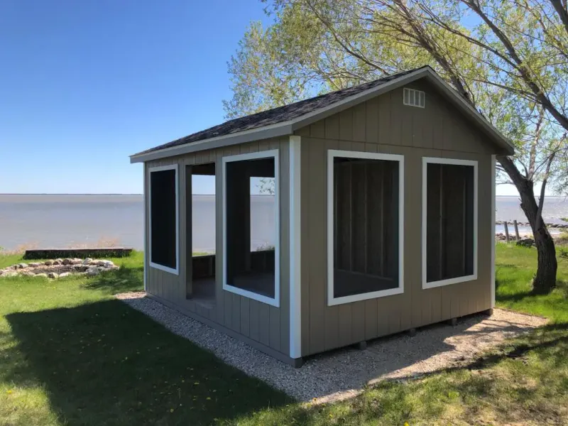 A screened shed near water with a tree nearby